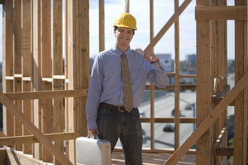 Fototapeta premium Portrait of a happy site manager with briefcase and blueprint with timber frames in background