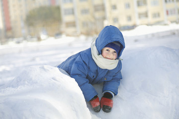 Fototapeta na wymiar Portrait of cute little boy in hooded jacket leaning on snow heap