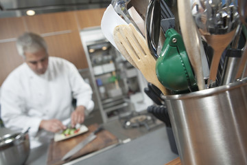 Male chef working with focus on utensil holder in foreground