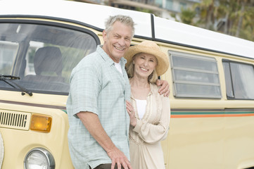Portrait of happy senior Caucasian couple standing together against campervan