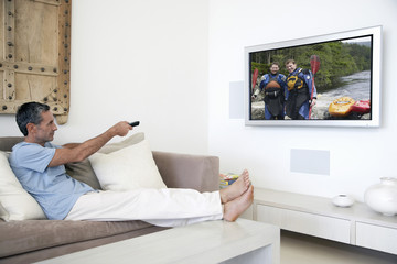Middle-aged man on sofa changing channels with television remote control