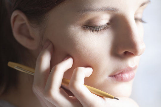 Closeup Of Thoughtful Young Woman With Pen Resting Hand On Chin