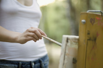Midsection of young woman painting on canvas in park