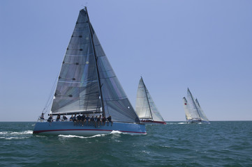 Overview of sailboats racing in the blue and calm ocean against sky