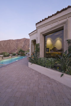 Paved poolside area and window exteriors of home against mountain and clear sky
