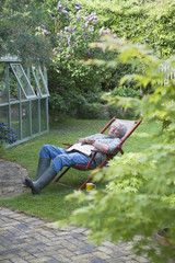 Full length of senior man sleeping on deckchair in backyard