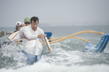 Confident male rower with team paddling outrigger canoe in race