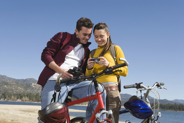 Young couple standing with mountain bikes looking at screen of camera