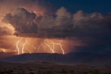 Electrical storm with forked lightning over the Grapevine mountains of the Amargosa Range, Mesquite Flats Sand dunes in the valley, Stovepipe Wells, Death Valley National Park, California