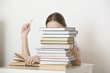 Young woman reading book behind stack of books at home