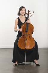 Portrait of a beautiful young woman playing cello against white wall © MDBPIXS