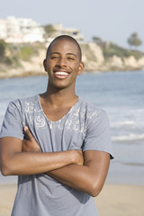 Portrait of a happy young African American man with arms crossed standing on beach