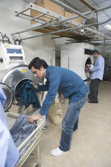 Fototapeta na wymiar Full length of young men loading clothes in washing machine at laundry