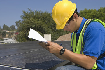Side view of young maintenance worker making notes near solar panels on rooftop