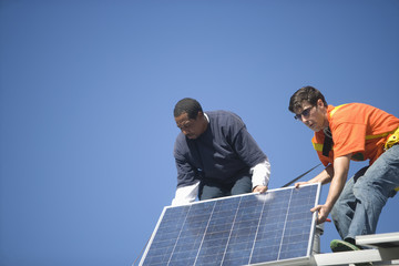 Low angle view of engineers fixing solar panel against blue sky