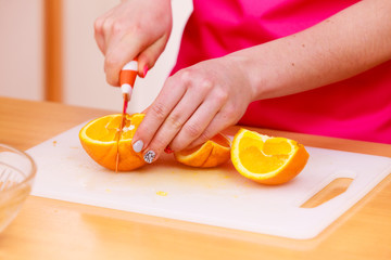 Woman housewife in kitchen cutting orange fruits