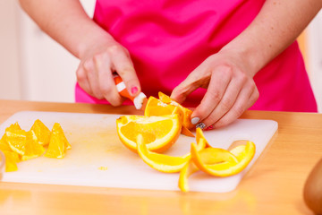 Woman housewife in kitchen cutting orange fruits