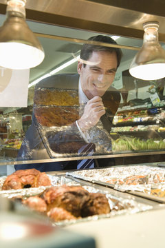 Mature Man Looks Through Glass Of Meat Counter In Supermarket