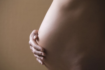 Midsection side view of pregnant woman touching tummy on colored background