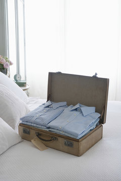 Ironed And Folded Shirts In Open Suitcase On Bed