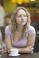 Thoughtful young woman with coffee cup leaning on table in shopping mall
