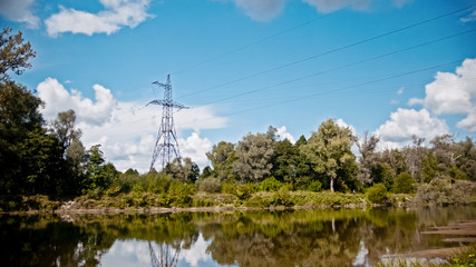 Wide shot timelapse of electricity power lines and high voltage pylons on a field in the countryside at summer near river - Powered by Adobe