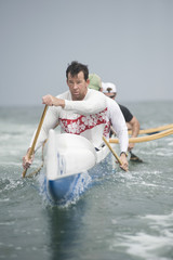 Confident male rower with team paddling outrigger canoe in race - obrazy, fototapety, plakaty