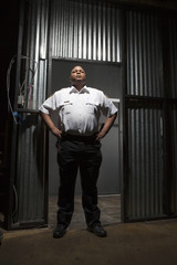 Fototapeta na wymiar Young confident security guard standing with hands on hip at corrugated doorway