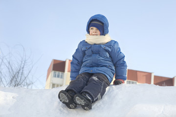 Fototapeta na wymiar Cute little boy in hooded jacket sitting on snow heap