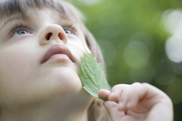 Closeup of cute girl looking up while touching leaf on face