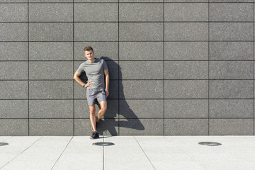 Full length portrait of confident sporty man leaning on tiled wall