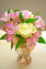 Colorful flowers in light pink colored vase with green leaves in the middle shot from the top using daylight, portrait composition