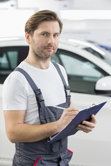Portrait of confident automobile mechanic writing on clipboard in workshop