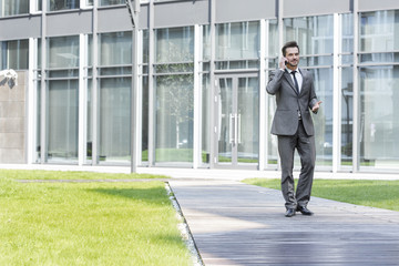 Fototapeta premium Businessman using cell phone while walking on path outside office