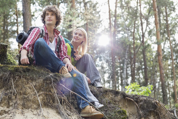 Naklejka na ściany i meble Young hiking couple sitting on edge of cliff in forest