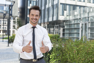 Fototapeta premium Portrait of confident businessman showing thumbs up outside office building