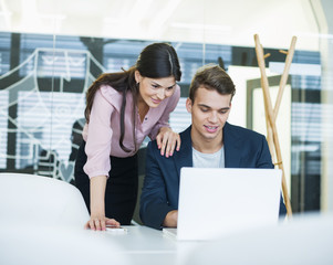 Young businessman and businesswoman using laptop at table in office