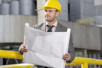 Young businessman holding blueprint while looking away at construction site