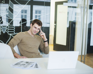 Fototapeta premium Handsome young businessman using smart phone in office