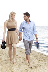 Full length of romantic young couple holding hands and walking on beach