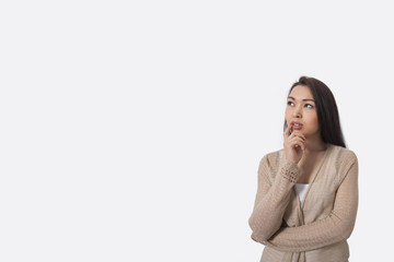 Thoughtful young woman standing against gray background