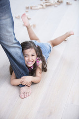 Fototapeta na wymiar Portrait of happy girl being dragged by father on hardwood floor