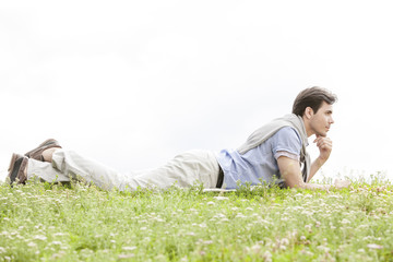 Full length of thoughtful young man lying on grass against clear sky