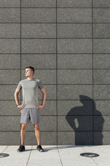 Determined jogger standing with hands on hips against tiled wall outdoors