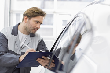 Fototapeta na wymiar Mid adult repair worker writing on clipboard while examining car in workshop