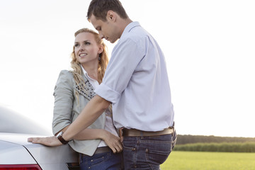 Romantic young couple leaning on back of car at countryside