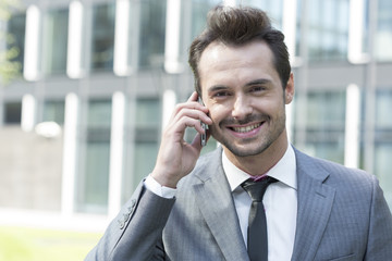 Portrait of happy businessman using cell phone outside office