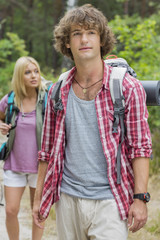 Naklejka premium Male backpacker looking away with woman standing in background at forest