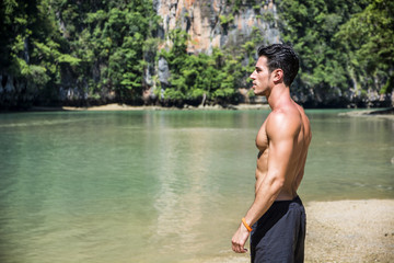 Fototapeta premium Half body shot of a handsome young man standing on a beach in Phuket Island, Thailand, shirtless wearing boxer shorts, showing muscular fit body