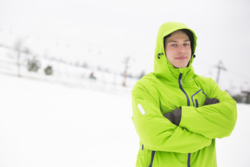 Portrait of young man in hooded jacket standing arms crossed in snow